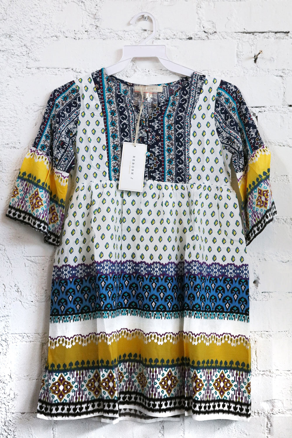 Colorful patterned dress on a hanger against a white brick wall.