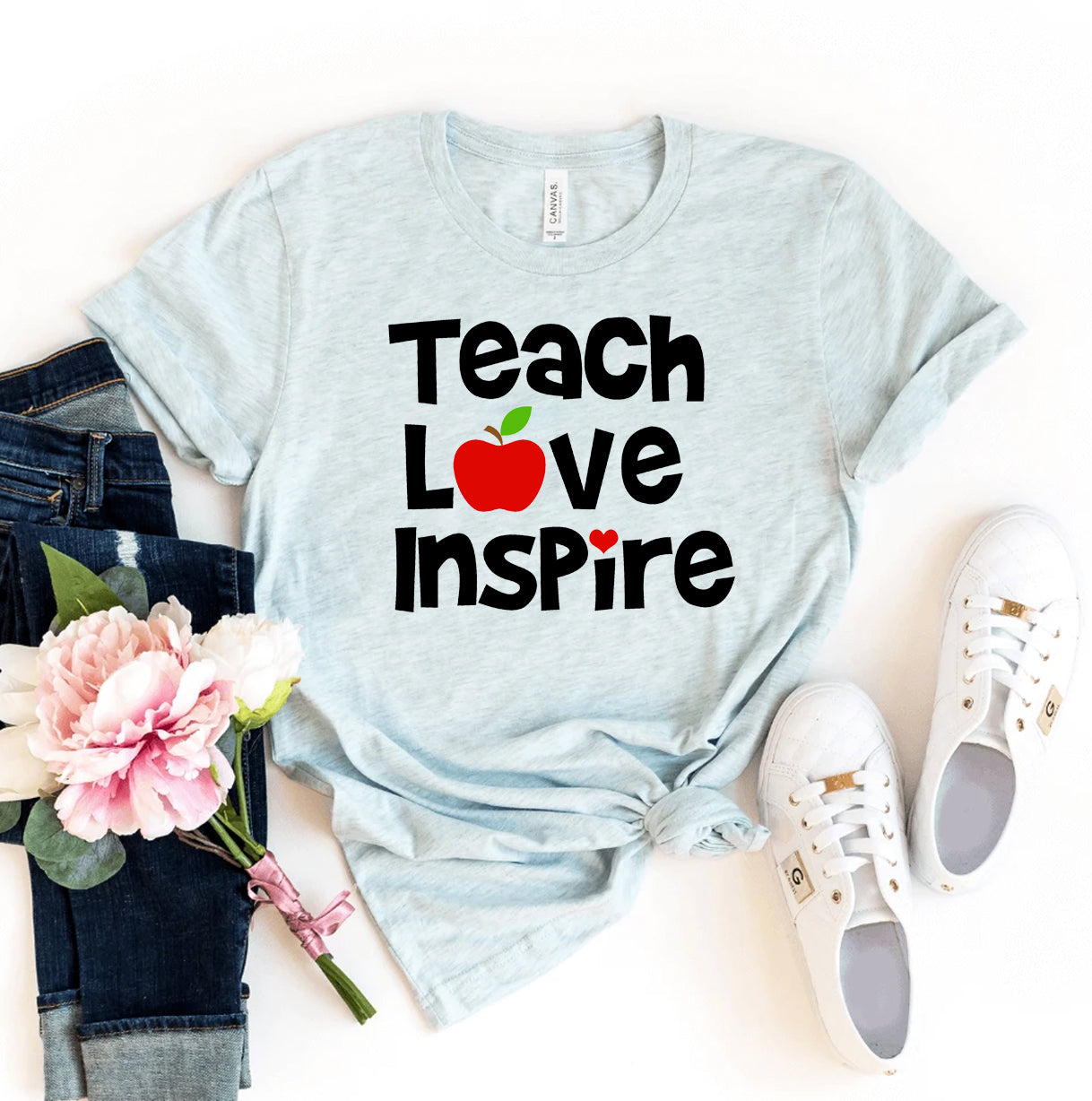 Light blue t-shirt with 'Teach Love Inspire' text, apple graphic, jeans, sneakers, and flowers on a white background