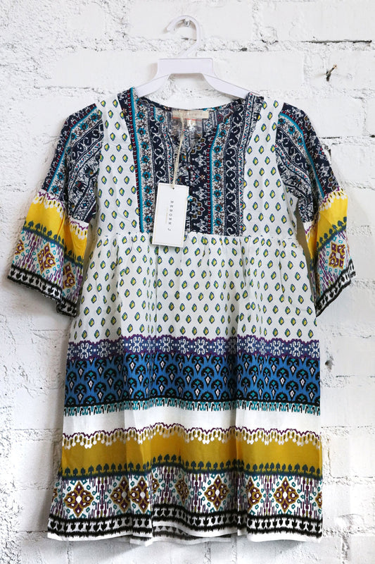 Colorful patterned dress on a hanger against a white brick wall.