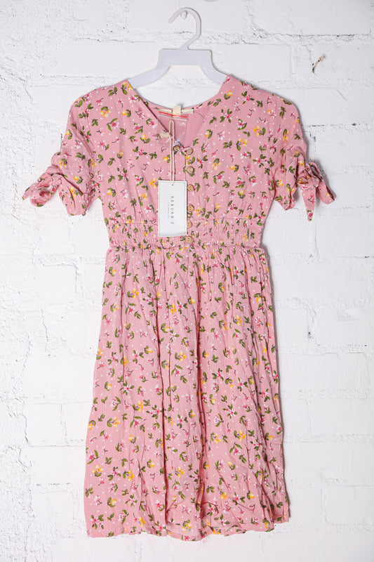 Pink floral dress on a hanger against a white brick wall