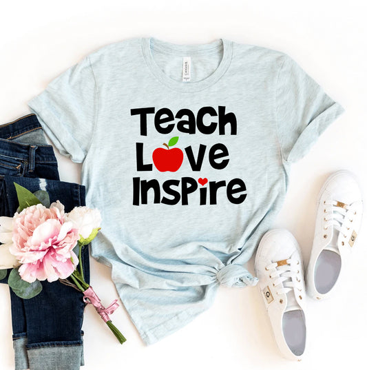 Light blue t-shirt with 'Teach Love Inspire' text, apple graphic, jeans, sneakers, and flowers on a white background