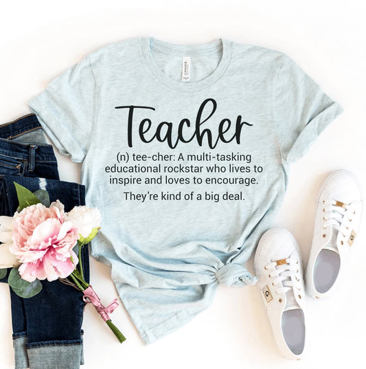 Light blue t-shirt with 'Teacher' definition text, jeans, sneakers, and flowers on a white background